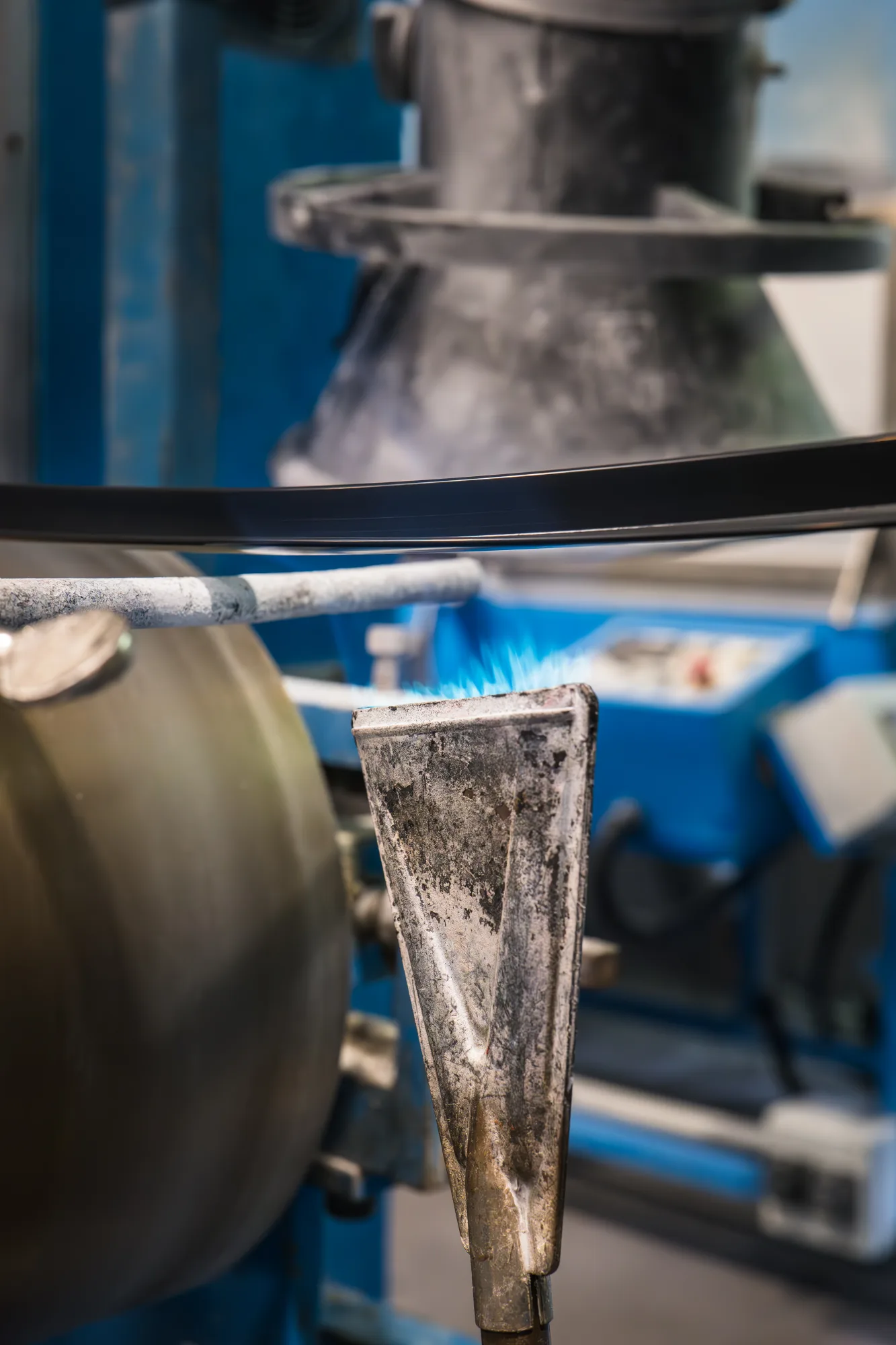 Calibrador de extrusión con llama piloto al fondo · taller industrial Apt