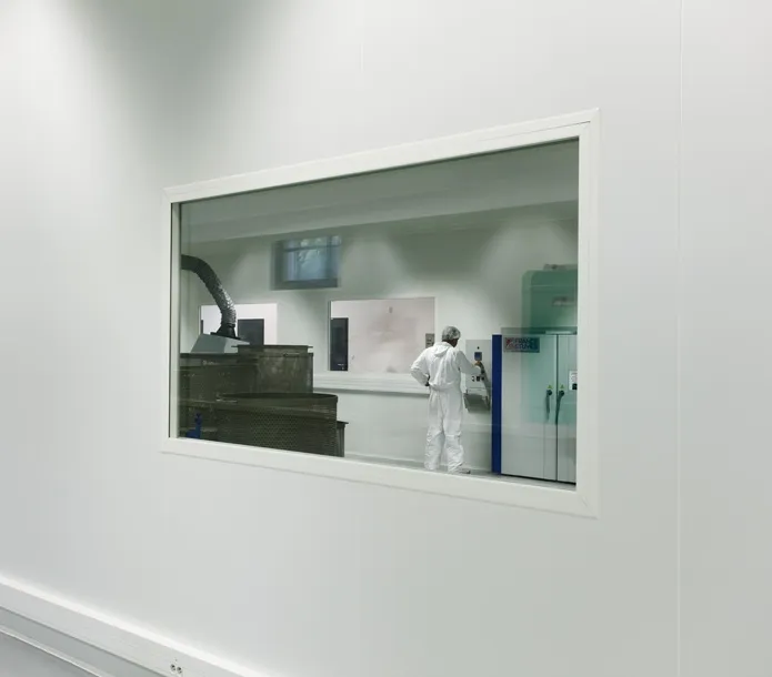 Mirador a la sala blanca ISO 8 con operario en buzo y autoclave verde · fabricación en entorno certificado