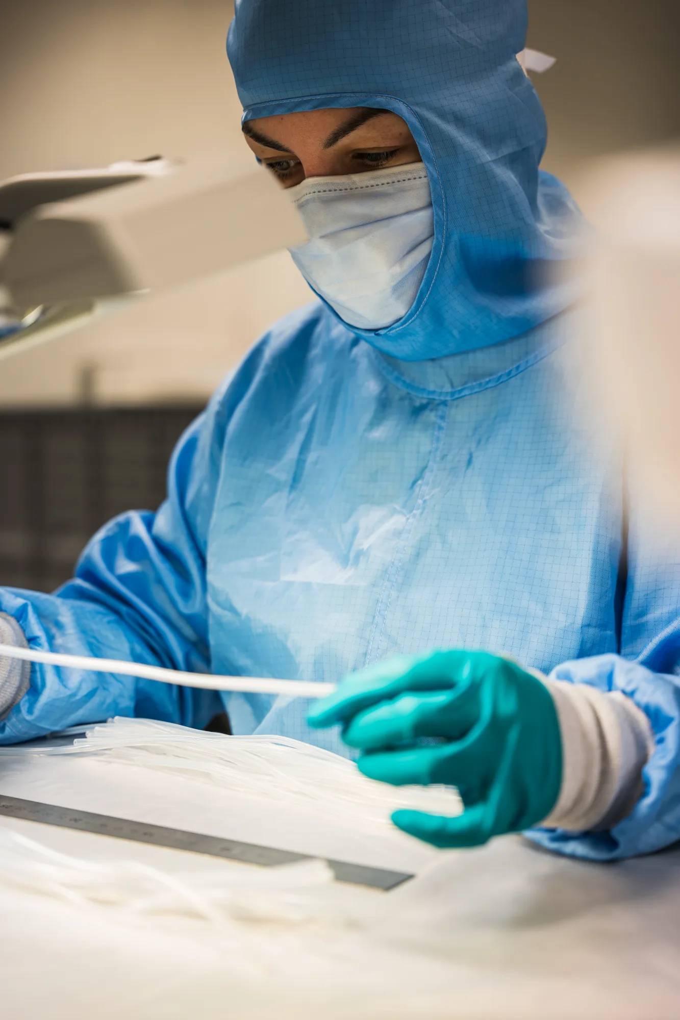 Técnica de sala blanca con guantes turquesa manipulando tubos médicos de silicona.